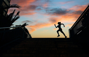 Unrecognizable young female runner silhouette running over an urban background with palm trees and...