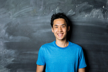 Happy Asian man standing next to a blackboard.