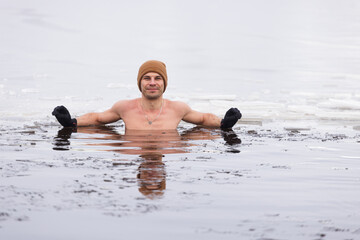 Engaging in winter swimming, a young man ventures into a frozen lake's ice hole, promoting wellness...