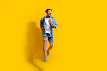 Fototapeta na wymiar Full body photo of pleasant man dressed denim shirt shorts run look at proposition empty space isolated on bright yellow color background