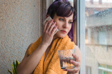 sporty young woman with mobile phone and glass of water looking out the window