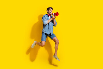 Fototapeta na wymiar Full size photo of cheerful guy wear jeans jacket jump look empty space announcing sale in loudspeaker isolated on yellow color background