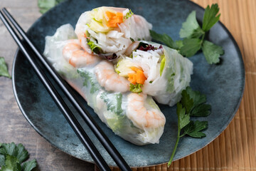Vietnamese spring rolls with vegetables, rice noodles and prawns on wooden table. Close up