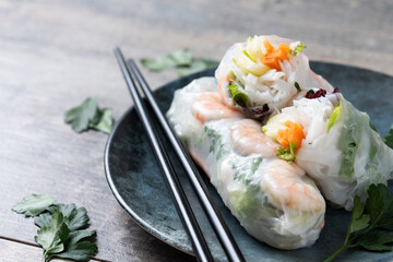 Vietnamese spring rolls with vegetables, rice noodles and prawns on wooden table. Copy space