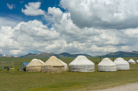 Scenic Kyrgyz yurts spread across Son-Kul's grassy plains with towering peaks and a vast sky enhancing the serene vista.