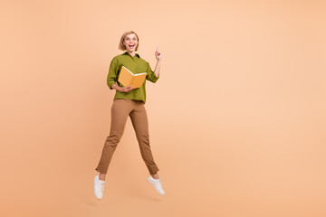 Fototapeta na wymiar Full length photo of ecstatic woman dressed green shirt brown pants flying hold book get great idea isolated on beige color background