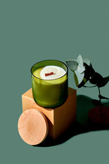 Creative minimalist composition with a candle with packing, eucalyptus on a green background. Mockup for candle makers.