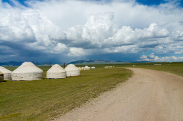 Traditional Kyrgyz yurts on Son-Kul's expansive pastures, encircled by distant mountains, cloud-streaked sky.