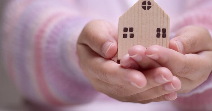 Detail of female hand holding small wooden block residence in hands - Real estate acquisition concept.