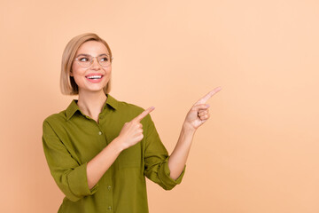 Photo of positive woman with bob hairstyle dressed green shirt indicating look at promo empty space isolated on beige color background