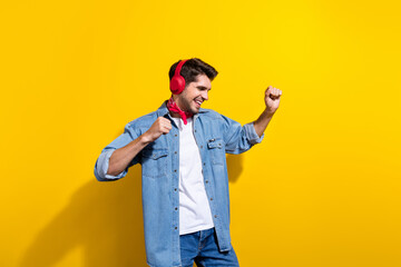 Photo portrait of handsome young guy listen music earphones have fun wear trendy jeans outfit isolated on yellow color background