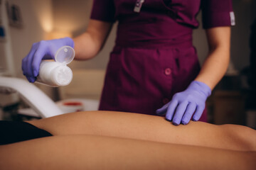 Cosmetologist sprinkling talcum powder on woman leg before the depilation procedure over white background
