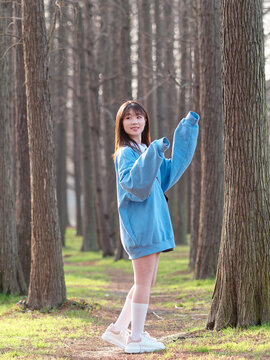 Beautiful young Chinese woman posing in sunny summer forest, wearing blue loose oversized top and miniskirt with small shoulder bag. Emotions, people, beauty, youth and lifestyle portrait.