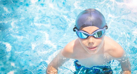 Fototapeta na wymiar Active, happy child (boy) in cap, sport goggles ready to learns professional swimming in swimming pool. Kid enjoying water. Healthy lifestyle. Copy space. =