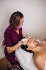 Fototapeta na wymiar Cosmetologist applying mask on man's face in spa salon,