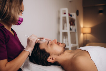 Obraz na płótnie Canvas Cosmetologist applying mask on man's face in spa salon,