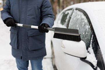 man holding brush and cleaning car after a snowfall