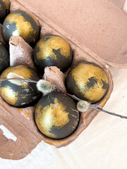 A small sprig of willow lies on the painted eggs in a cosmic gold color. An Easter card. Vertical photo