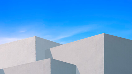 Sunlight and shadow on surface of white concrete building wall against blue sky background,...