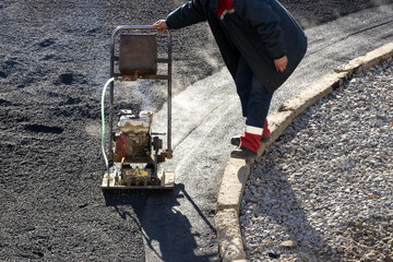 Asphalt compactor compress. A worker of the road service rams asphalt with a portable machine for tamping asphalt. - obrazy, fototapety, plakaty