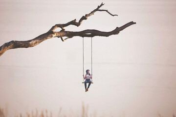 surreal woman swings on a swing hanging from a branch, concept of freedom and precariousness - obrazy, fototapety, plakaty