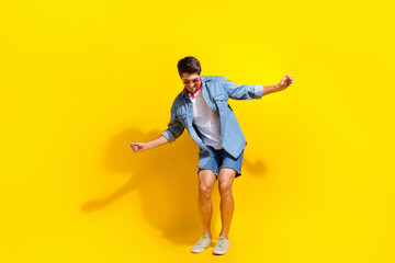 Fototapeta na wymiar Full size photo of funky cheerful guy wear jeans jacket shorts in sunglass dancing near empty space isolated on yellow color background