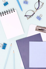 School supplies and eyeglasses on a blue background. Blank notepad.