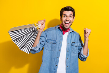 Photo of overjoyed guy with bristle wear jeans jacket hold shopping bags clenching hand celebrate...
