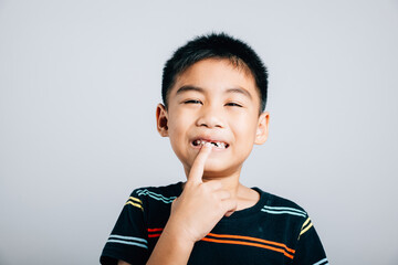 Child an Asian boy points to missing front tooth symbolizing dental care. Isolated on white...
