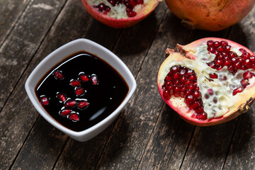Pomegranate molasses in small bowl on rustic wooden table. Pomegranate sweet and sour syrup with pomegranate fruit and seeds.