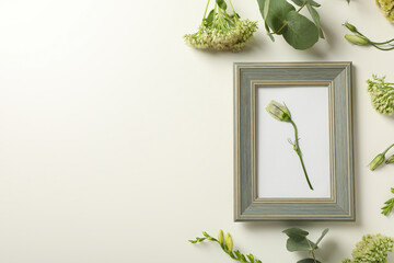 Photo frame and fresh flowers on light background, space for text