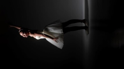 Graceful ballet dancer performing in pointe shoes under spotlight. Flexible ballerina dancing in tutu skirt on dark stage. Sensual female person enjoying classical dance indoors.