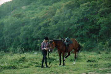 Happy blonde with horse in forest. Woman and a horse walking through the field during the day. Dressed in a plaid shirt and black leggings.