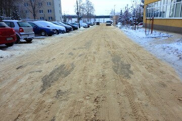 Asphalt road with a lot of snow sprinkled with sand in a housing estate
