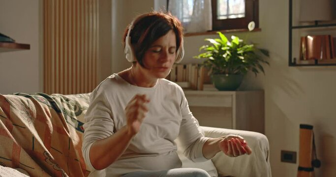 At home, a middle-aged woman sits on the sofa, puts on headphones and puts on music that makes him dance, have fun and let loose.
The elderly woman dances and  play imaginary musical instruments