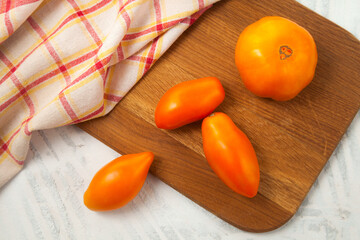 Cutting board with several yellow tomatoes and red kitchen towel on white wooden background..