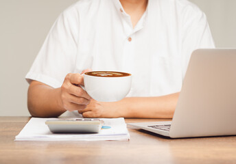 Businessman holds a cup of coffee while sitting at a desk in the office.