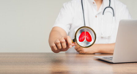 Doctor holds a magnifying glass with a red lung icon while sitting at a desk in the hospital.