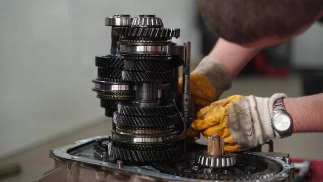 Auto mechanic repairs gearbox, hands work on vehicle transmission in service shop. Car maintenance, fix gears, manual clutch assembly, professional automotive overhaul, auto parts replacement.