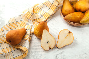 Whole and halves of pears, wicker basket and yellow kitchen towel on white wooden background..