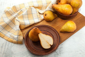 Clay plate with whole and half of pear, wicker basket and yellow kitchen towel on wooden cutting board..