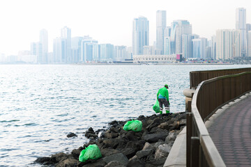  worker in uniform clean up garbage on the shore of the sea bay in the early summer morning.