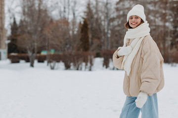 Obraz premium Young adult caucasian woman dressed coat scarf hat and mittens enjoys winter weather at white snowy winter park