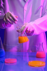 Research science concept with a scientist standing and stirring the orange liquid inside a conical flask. Blue table featured few flasks and glass petri dish of colorful liquid