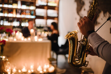 Saxophonist's hands while playing jazz. Musician hold sax at romantic date on Valentine's Day in restaurant. Man performing on saxophone at party or wedding. Jazz music concept closeup. Space for text - obrazy, fototapety, plakaty