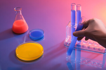 A hand with medical glove holding a test tube with blue chemical liquid. An erlenmeyer flask and...