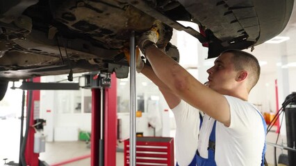 Auto mechanics in uniform install gearbox, repair car clutch in modern workshop. Professionals work on vehicle transmission maintenance with tools, demonstrate mechanical skills under raised auto.