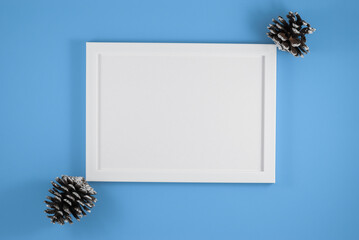 White frame and pine cones on blue background. Flat lay. Party mockup. Invitation or greeting card
