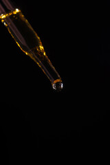 Glass pipette for cosmetics. A drop of cosmetics oil on a black background close-up macro