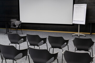 Empty conference room with rows of  grey chairs, media screen and whiteboard.